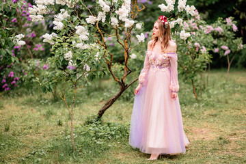 Obraz na płótnie Canvas Beautiful romantic fairy girl in long dress in blooming spring garden. Gorgeous young model with perfect hairstyle in fairy forest. Fantasy art