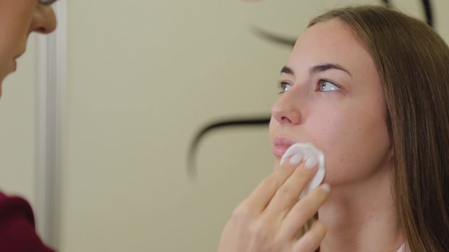 Professional make-up artist wipes face of client with cotton swabs.