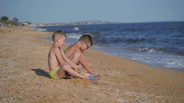 Rest on the sea with children. The boys throw up a shell with sand. Children's emotions. Boys throw sand.