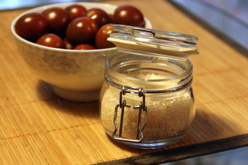 Small dark tomatoes in a white bowl and a glass jar with rice on a table