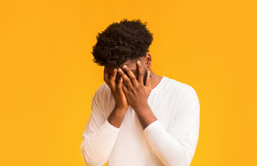 Young afro guy covering his face with both hands