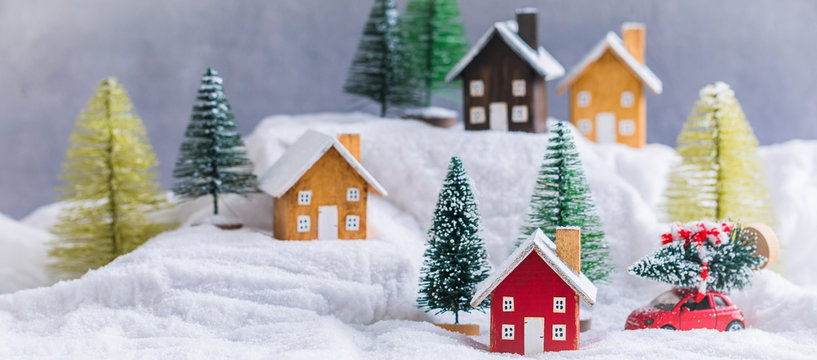 Miniature wooden houses village on the snow over blurred Christmas decoration background, toned, banner