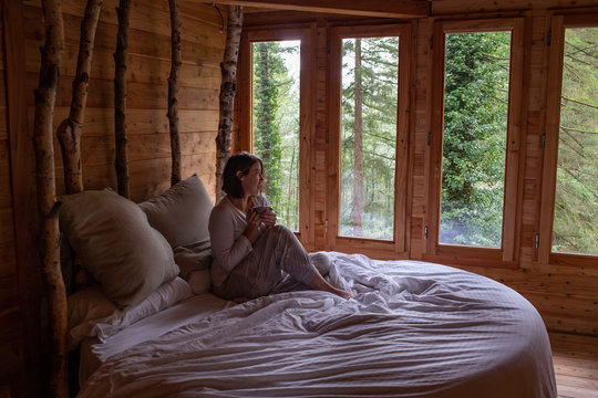 beautiful young woman sitting on the bed and drinking coffee in a tree house. Otzarreta, Basque Country, Spain