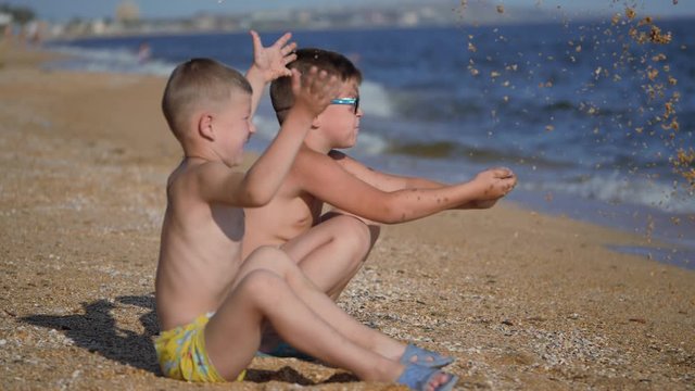 Rest on the sea with children. The boys throw up a shell with sand. Children's emotions. Boys throw sand.