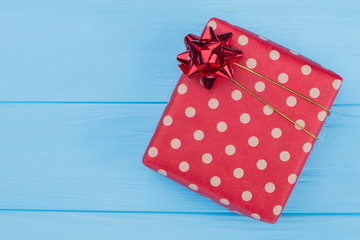 Gift box wrapped in dotted red paper. Top view. Blue wood background.