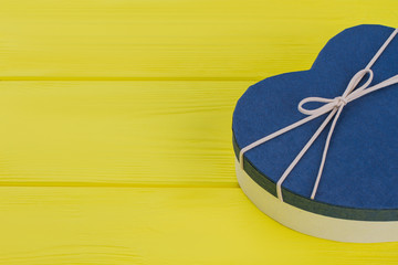 Blue heart-shaped gift box on yellow wood. Close up. Top view.