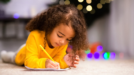Fototapeta na wymiar Cute african little girl writing on floor near Christmas tree