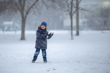 Fototapeta na wymiar A little boy in a hat and jacket laughs and rejoices in the winter snow .