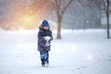 A little boy in a hat and jacket laughs and rejoices in the winter snow .