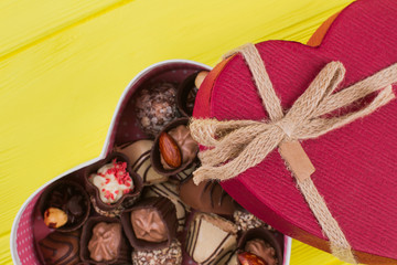 Red heart shaped gift box with chocolate candies. Assorted Chocolates on yellow wooden background. Valentines Day gift.