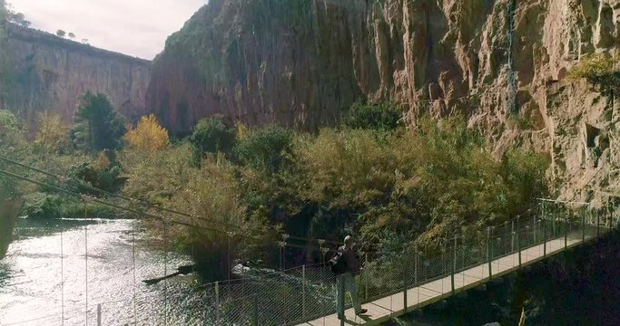Vuelo ascendente de dron y anciano caminante cruza un puente colgante