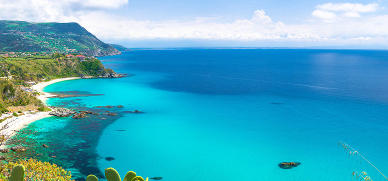 Aerial amazing tropical panoramic view of turquoise gulf bay, sandy beach, green mountains and plants, blue sky white clouds background, cliffs platform Cape Capo Vaticano, Calabria, Southern Italy