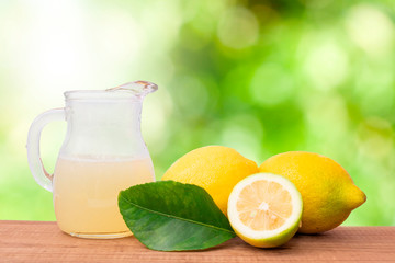 natural lemons with jug of lemon juice on natural background