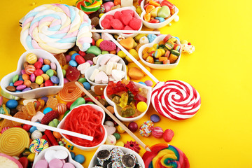 candies with jelly and sugar. colorful array of different childs sweets and treats on yellow background