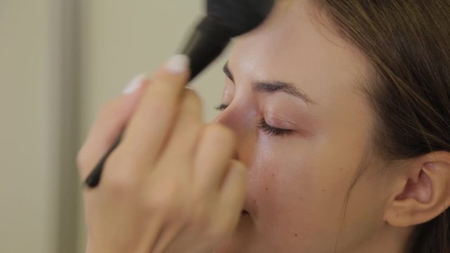 Professional makeup artist is applying powder to the client's face with a brush.