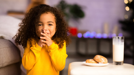 Cute little african girl preparing milk and cookies for Santa Claus