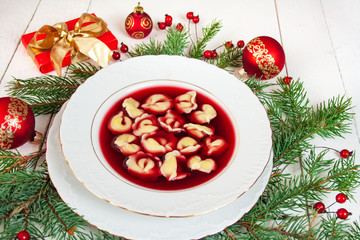 Fototapeta na wymiar Traditional Polish Christmas Eve dish - red borscht with dumplings, spruce branches, gifts and red baubles in the background