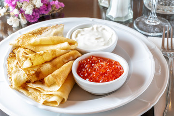 Fried crepes with caviar and sour cream on the white dish served in the restaurant.
