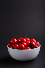 Fresh red sweet cherry in white bowl on black background. side view.