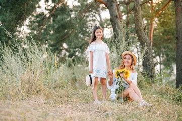 Cheerful mother and her little daughter having fun together in the summer background. Happy family in the nature background. Cute girls with colorful flowers.