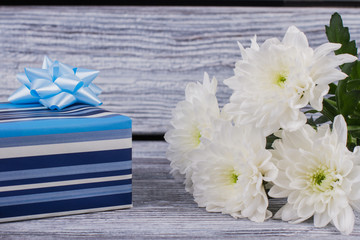 Blue gift box and white chrysanthemums. White flowers and present box on vintage wooden background. Happy Birthday card.