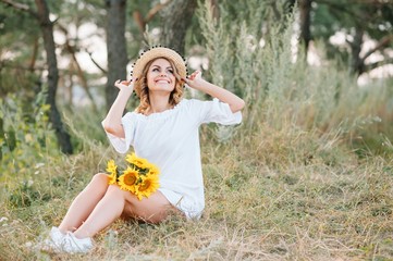 Outdoor shot of pleasant looking female with tanned healthy skin, dressed in white dress and summer hat, poses in park with confident satisfied expression, likes recreation. Beautiful young woman