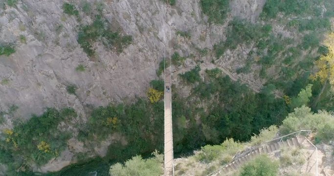 Senior cruza un puente colgante  sobre barranco y el dron graba en cenital
