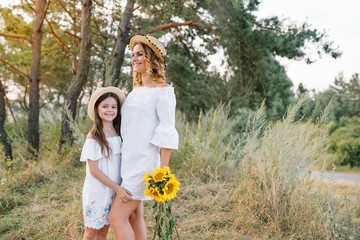 Cheerful mother and her little daughter having fun together in the summer background. Happy family in the nature background. Cute girls with colorful flowers.