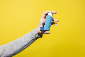 Close-up of female hand holding asthmatic inhaler on yellow background.