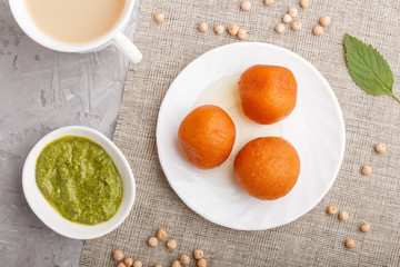 traditional indian candy gulab jamun in white plate with mint chutney on a gray concrete background. top view.