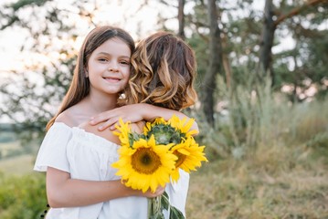 Cheerful mother and her little daughter having fun together in the summer background. Happy family in the nature background. Cute girls with colorful flowers.