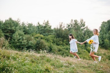 Fototapeta premium Cheerful mother and her little daughter having fun together in the summer background. Happy family in the nature background. Cute girls with colorful flowers.
