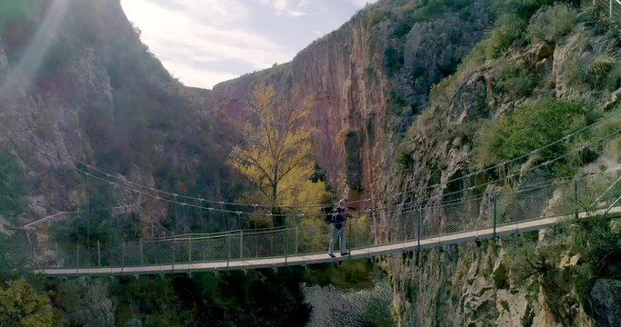 vuelo hacia atr&aacute;s de dron grabando un viejo de barba blanca caminado sobre un puente colgante