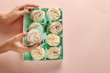 Box with homemade marshmallows in female hands on a pastel background, Top view, Copy space