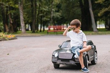 Cute boy in riding a black electric car in the park. Funny boy rides on a toy electric car. Copy space.