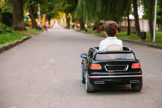 Cute boy in riding a black electric car in the park. Funny boy rides on a toy electric car. Copy space.