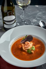 Fresh seafood soup in a white plate on dark background, top view