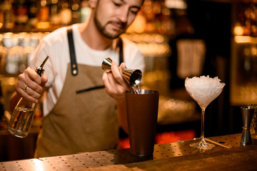 Bartender pouring a alcoholic drink from the jigger to a steel shaker