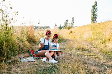 Sunny nature, mom and daughter paint a picture in a park , painting a Little Child, Child Creativity. Mother's Day