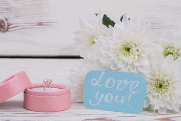 Obraz na płótnie Canvas Diamond ring and bouquet of flowers. Romantic background with engagement ring in gift box and white chrysanthemum flowers on wooden background. Valentines Day concept.