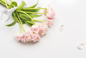 High angle view of pink ruffled tulips tied with ribbon with falling petals on white background
