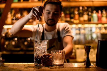 Bartender stirring a brown alcoholic drink with a spoon in the mixing glass