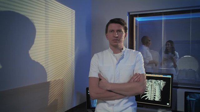 A picture of a male doctor. The doctor is standing in the tomography room, he smiles and looks at the camera. Professional people at work.