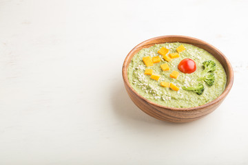 Green broccoli cream soup in wooden bowl on a white wooden background. side view, copy space.