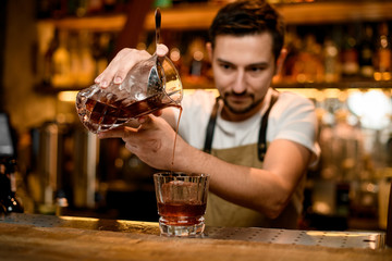 Bartender pouring a brown alcoholic drink from mixing glass to a cocktail glass with ice cube