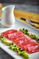 Slices of raw tuna sashimi served on white board with avocado