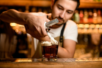 Professional bartender adding whipped cream to a brown cocktail in the glass