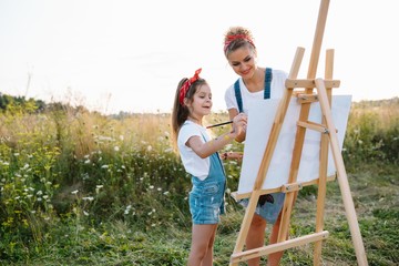 mother teaches daughter paint in park. Sunny nature, mom and daughter paint a picture in a park , painting a Little Child, Child Creativity. Mother's Day