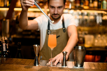 Professional male bartender adding with tweezers a little sugar cube to a cocktail in the glass
