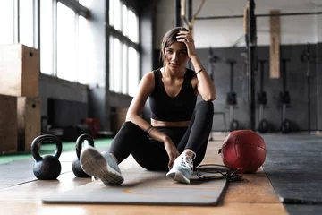 Foto op Plexiglas Jonge vrouw zittend op de vloer na haar training en naar beneden te kijken. Vrouwelijke atleet die rust neemt na fitnesstraining © opolja